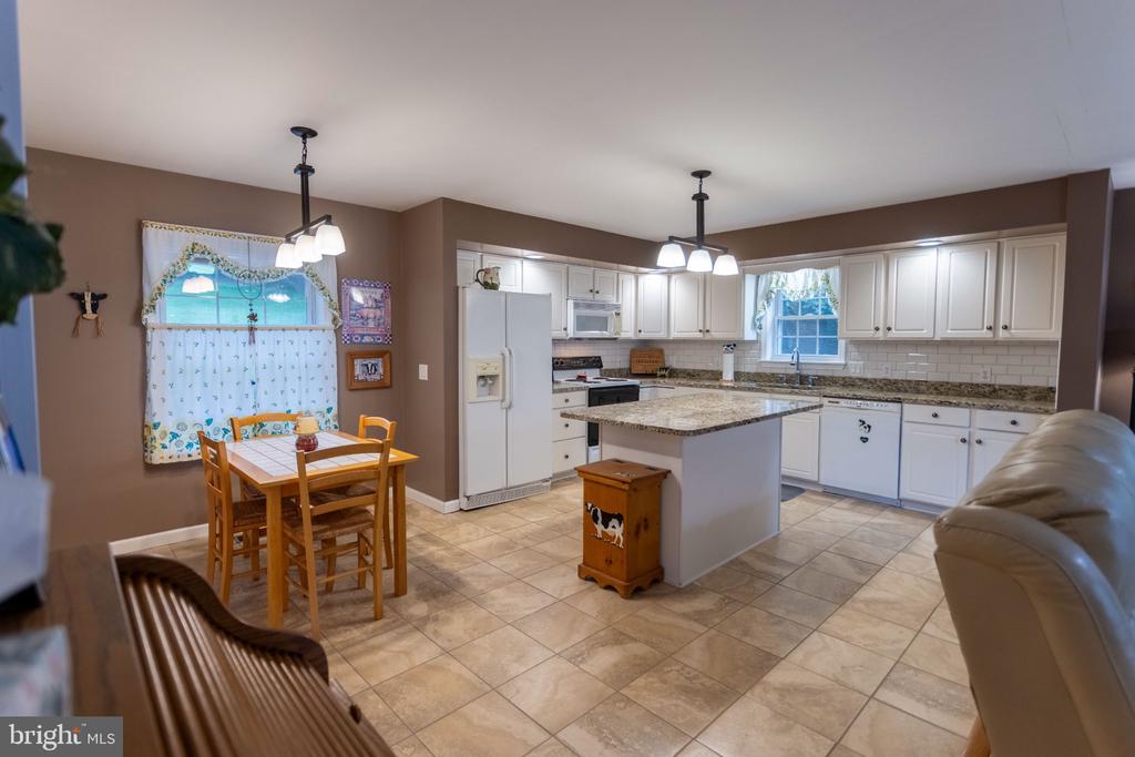 Kitchen with white cabinets, granite island, tiled floors, and an adjoining wooden dining area.