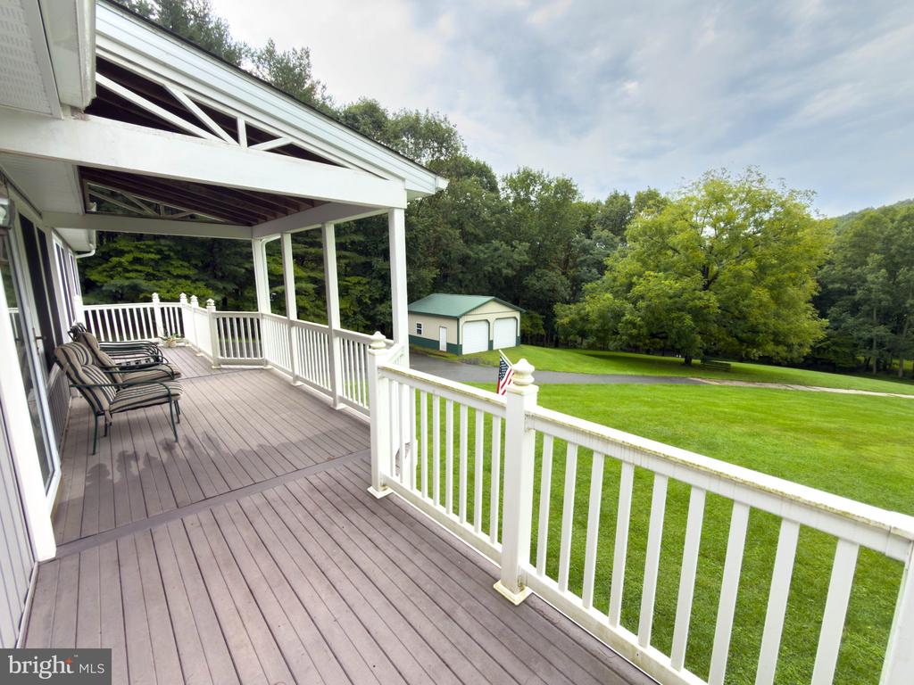 Covered deck with white railings and seating overlooking a green lawn and detached outbuilding.