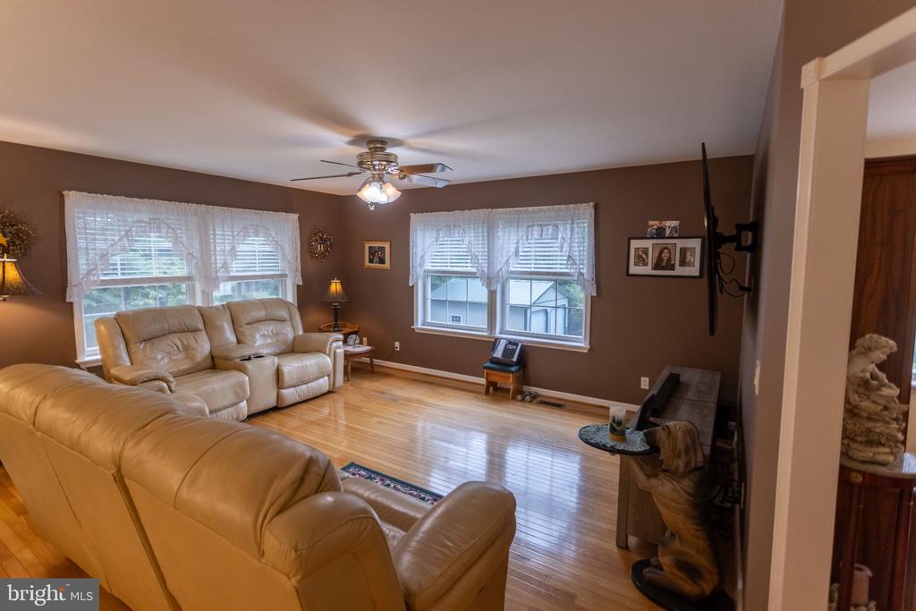 Living room with tan leather sofas, hardwood floors, and windows with sheer curtains.