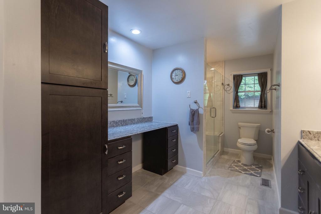 Bathroom with dark wood cabinetry, stone counters, and a glass-enclosed shower beside a curtained window.