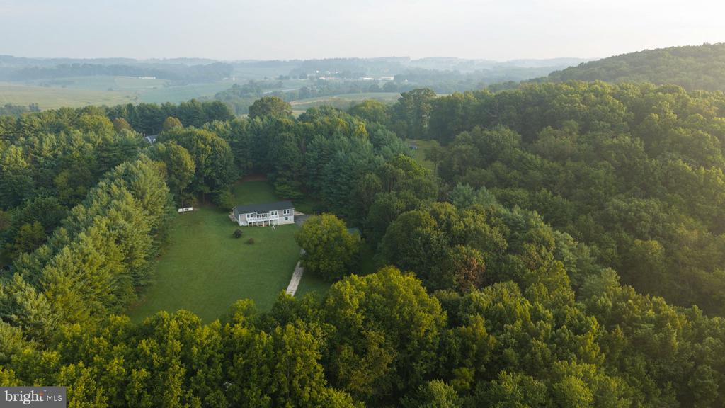 Aerial view of a secluded house in a wooded clearing amid rolling countryside.
