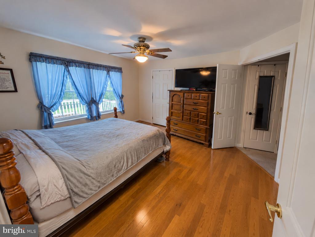 Bedroom with blue window curtains, a large bed, hardwood floors, and a television on a wooden dresser.