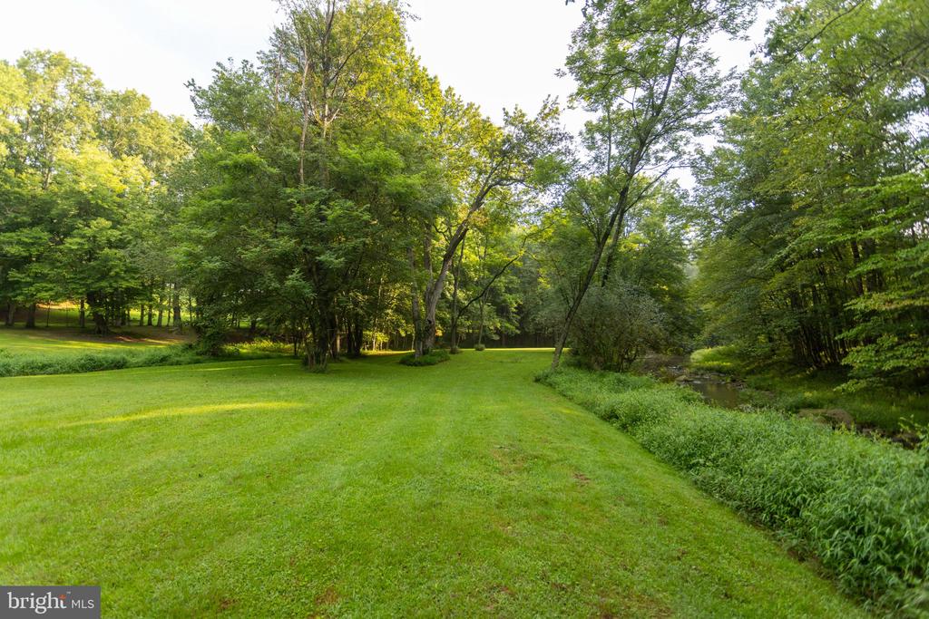 Grassy property grounds with mature trees and a creek along the right side.