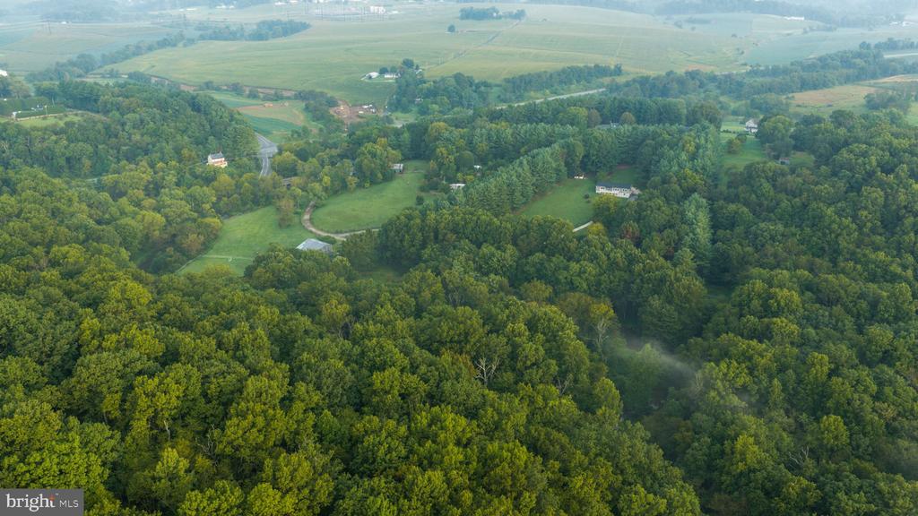 Aerial view of wooded acreage with open fields and scattered homes.
