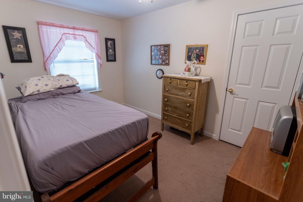 Bedroom with a wooden bed, pink window curtains, and a wooden chest of drawers.
