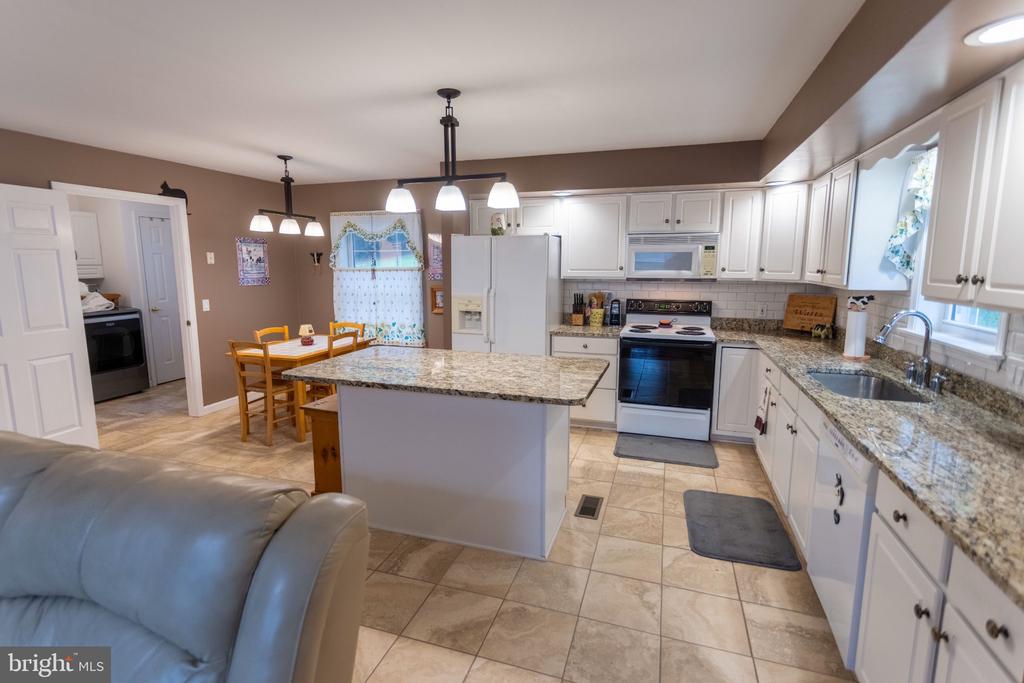Kitchen with a granite island, white cabinetry, and a dining area beside the living room.