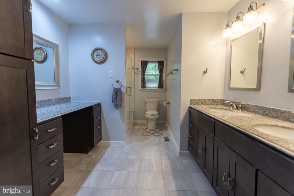 Bathroom with long double vanities, granite counters, and a glass shower beside a separate toilet alcove.
