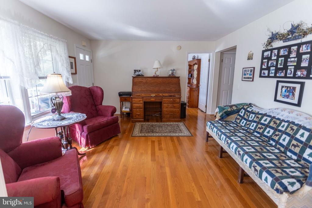 Living room with burgundy armchairs, patterned sofa, wooden desk, and hardwood floors.