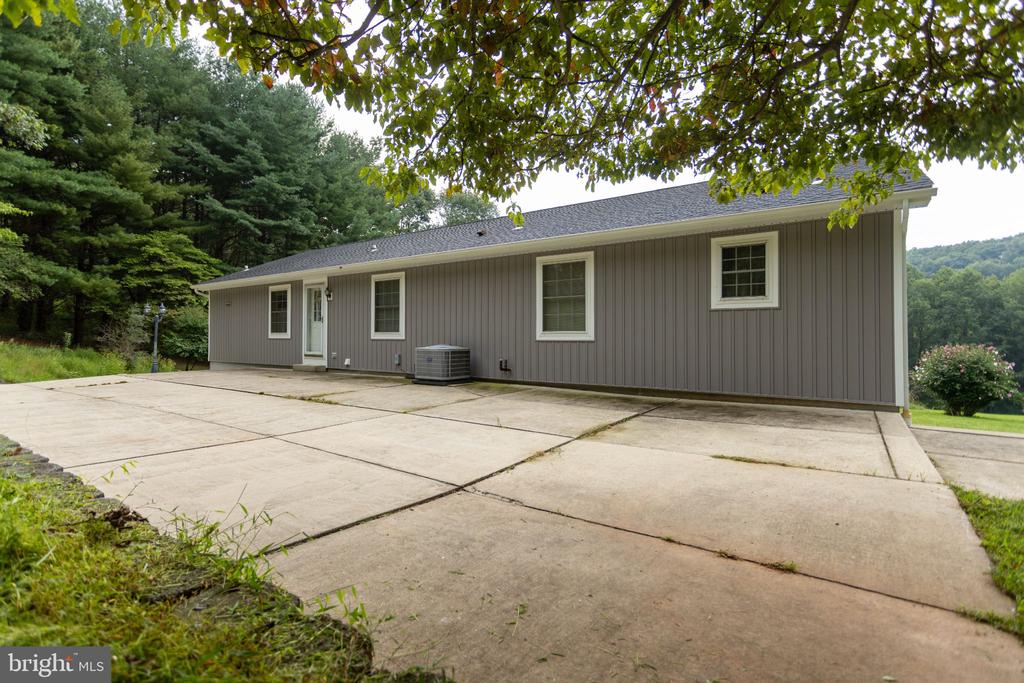 Single-story gray-sided house beside a broad concrete driveway, shaded by mature trees.