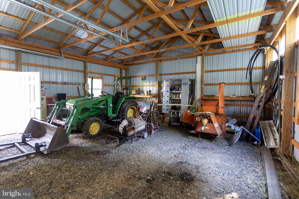 Barn interior with a green tractor, front loader, and assorted farm equipment.