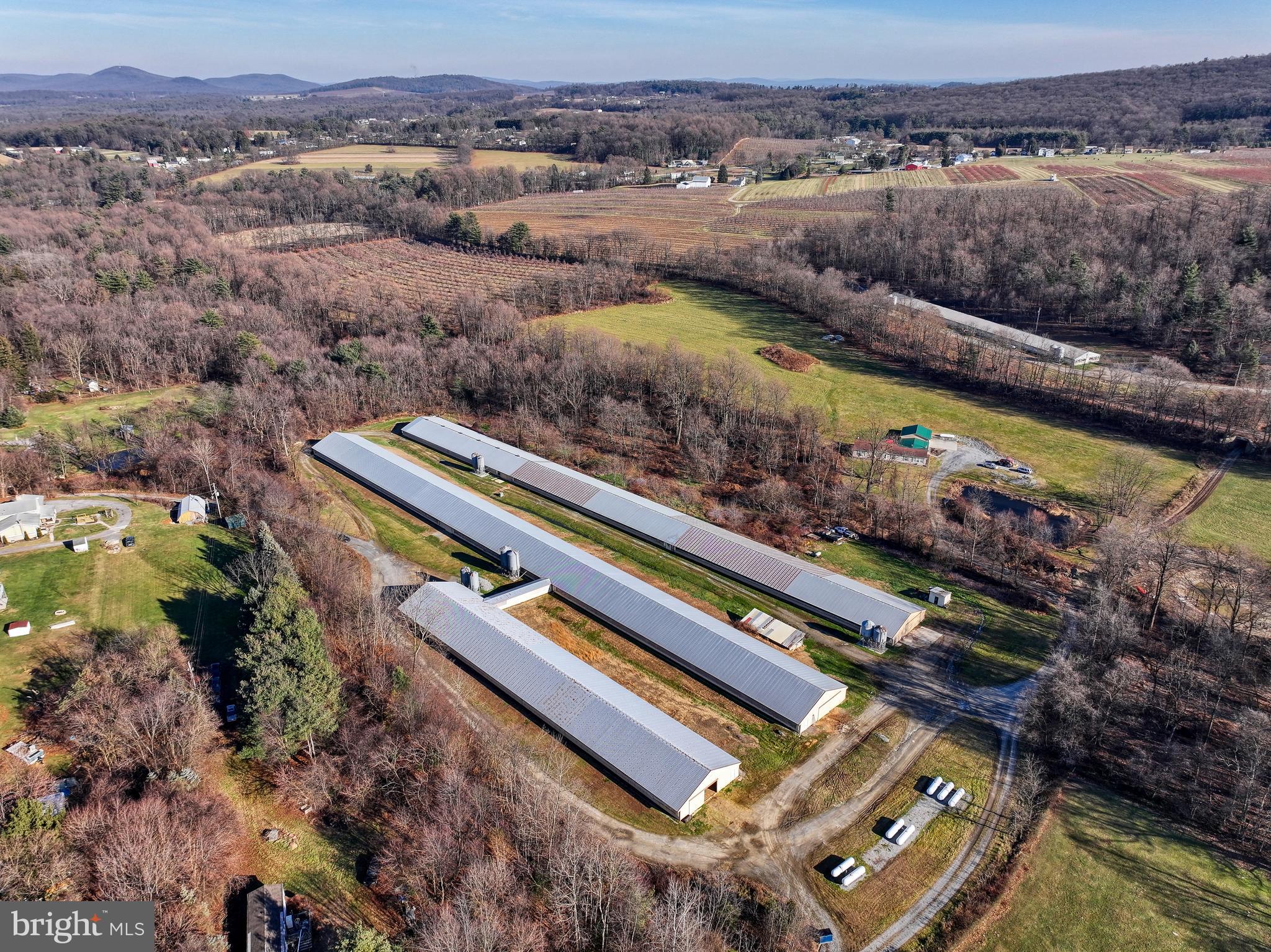 Rural property with long poultry barns, open fields, and wooded hills.