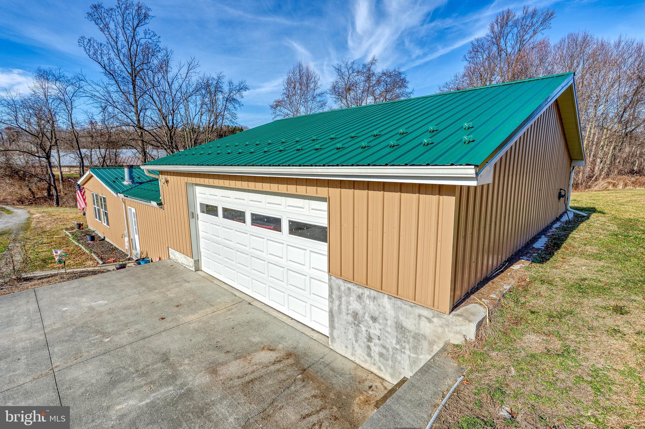 Tan garage building with a green metal roof, white overhead door, and wide concrete driveway.