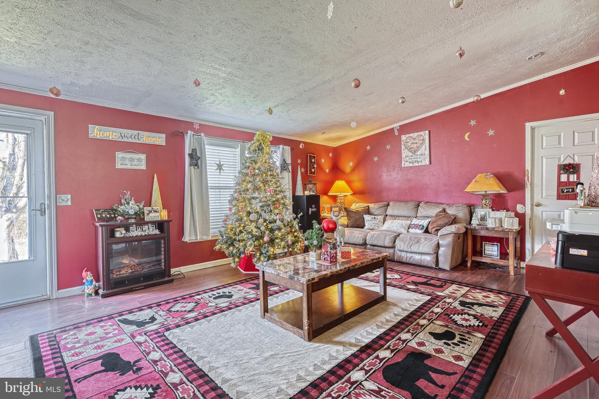 Living room with red walls, a decorated Christmas tree, beige reclining sofa, and electric fireplace.