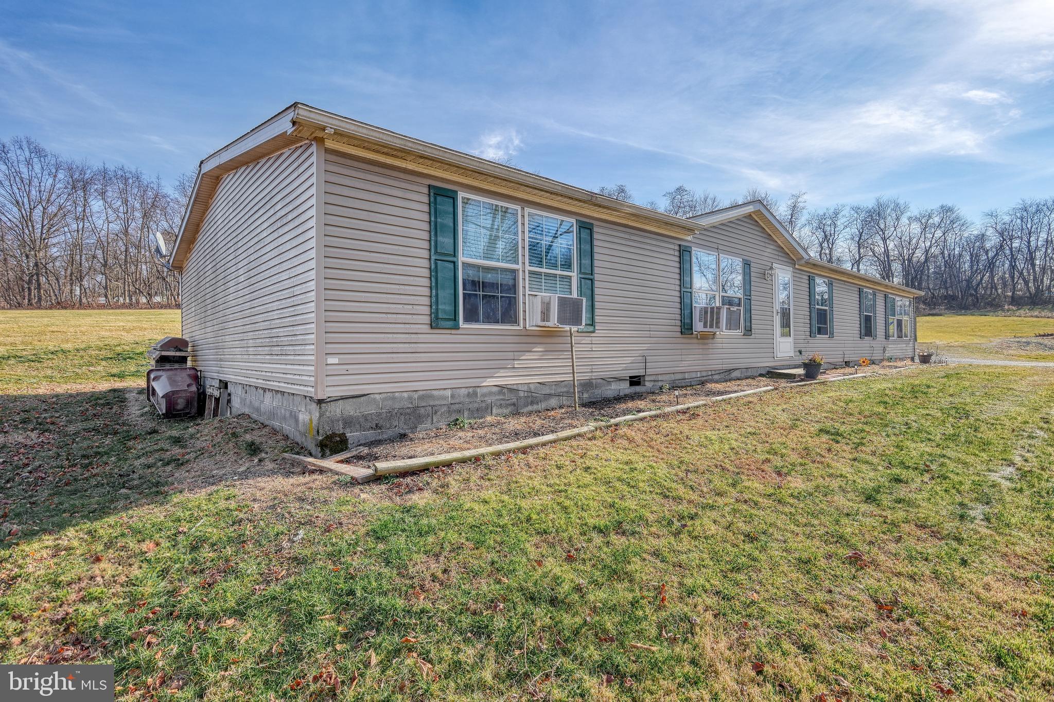 Beige manufactured home with green shutters and window air conditioners in a grassy yard.