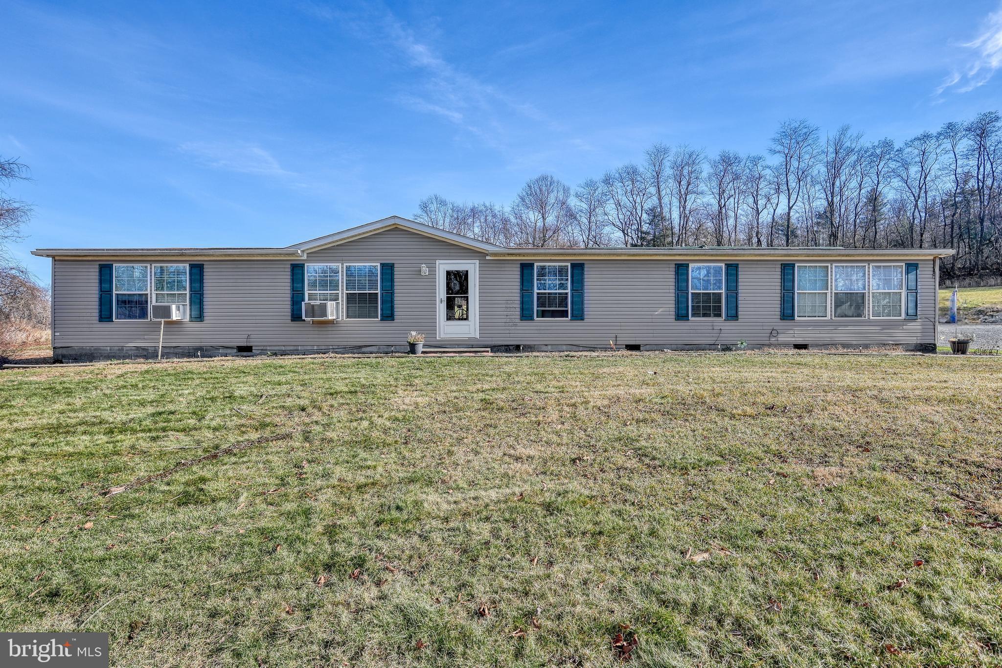 Long gray single-story home with blue shutters and a broad front lawn.