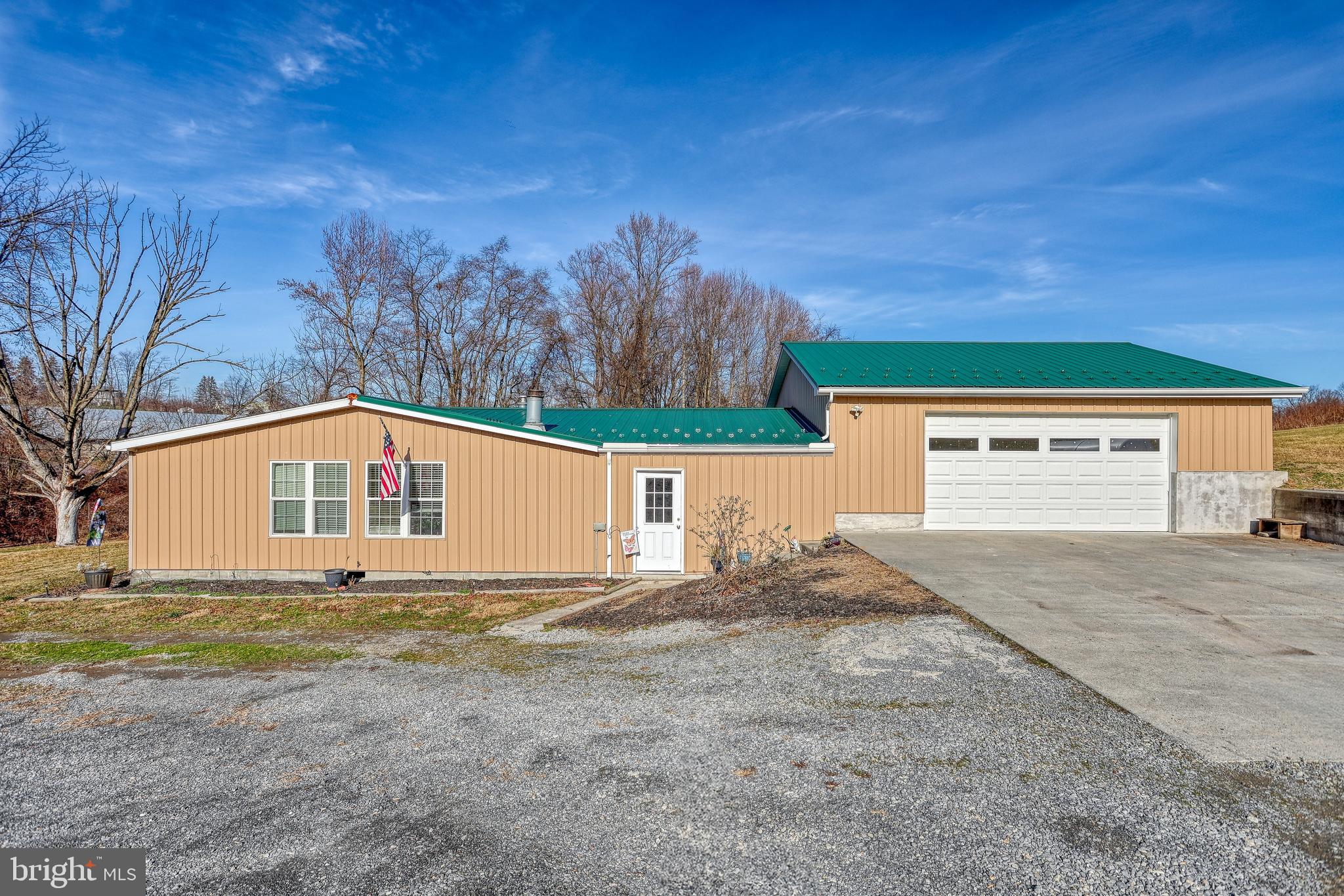 Tan-sided home with green metal roofs, attached garage, and broad driveway.