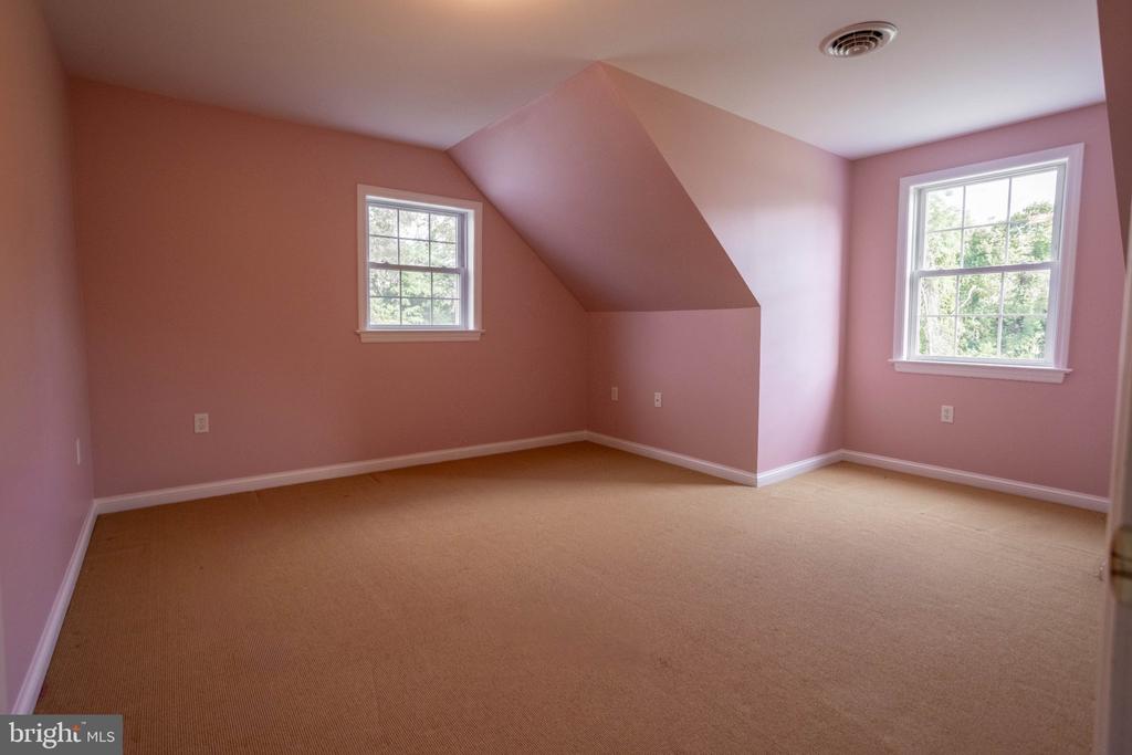 Empty bedroom with pink walls, beige carpet, two windows, and an angled ceiling.