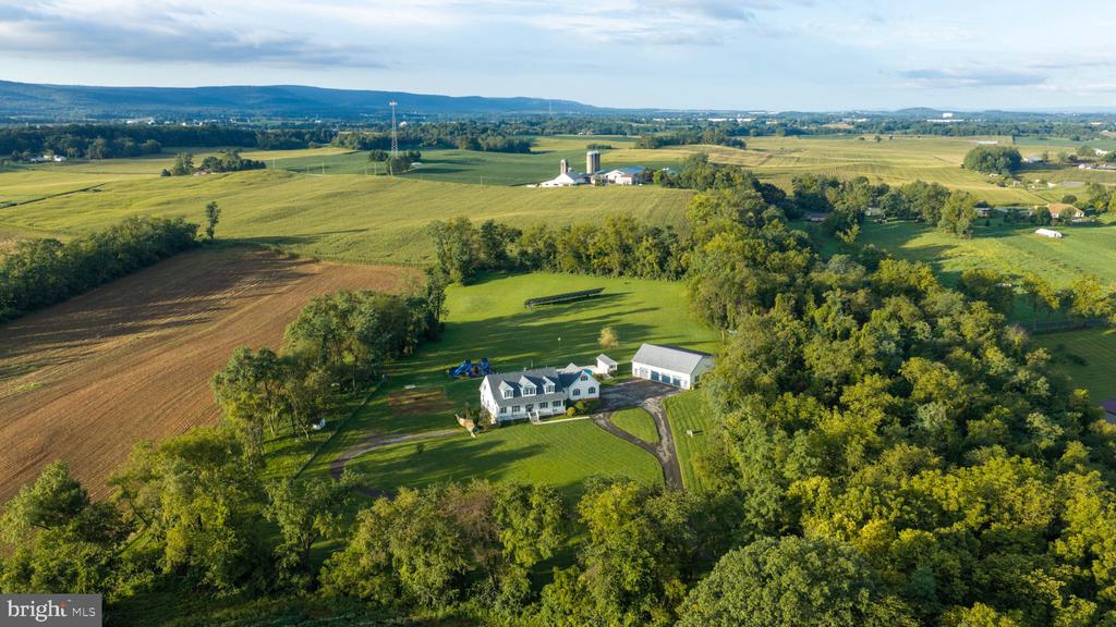 Aerial view of a white house, driveway, outbuilding, and surrounding green farmland.