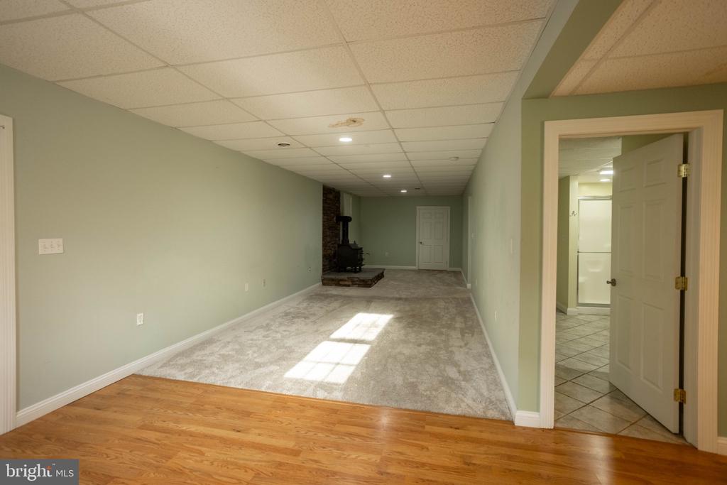 Finished basement with a wood stove, carpeted floor, and hardwood flooring in the foreground.