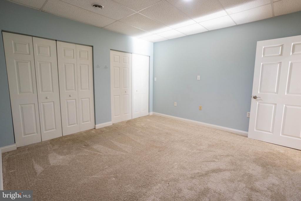 Empty bedroom with beige carpet, pale blue walls, and multiple white closet doors.