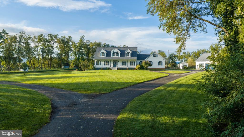 White two-story house with dormers, a broad lawn, and a curving driveway to a detached garage.