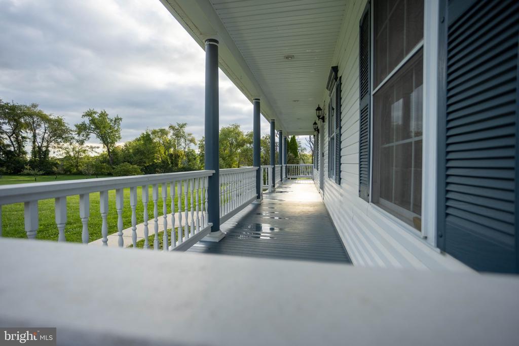 Covered porch with gray columns and white railing overlooking a green lawn.