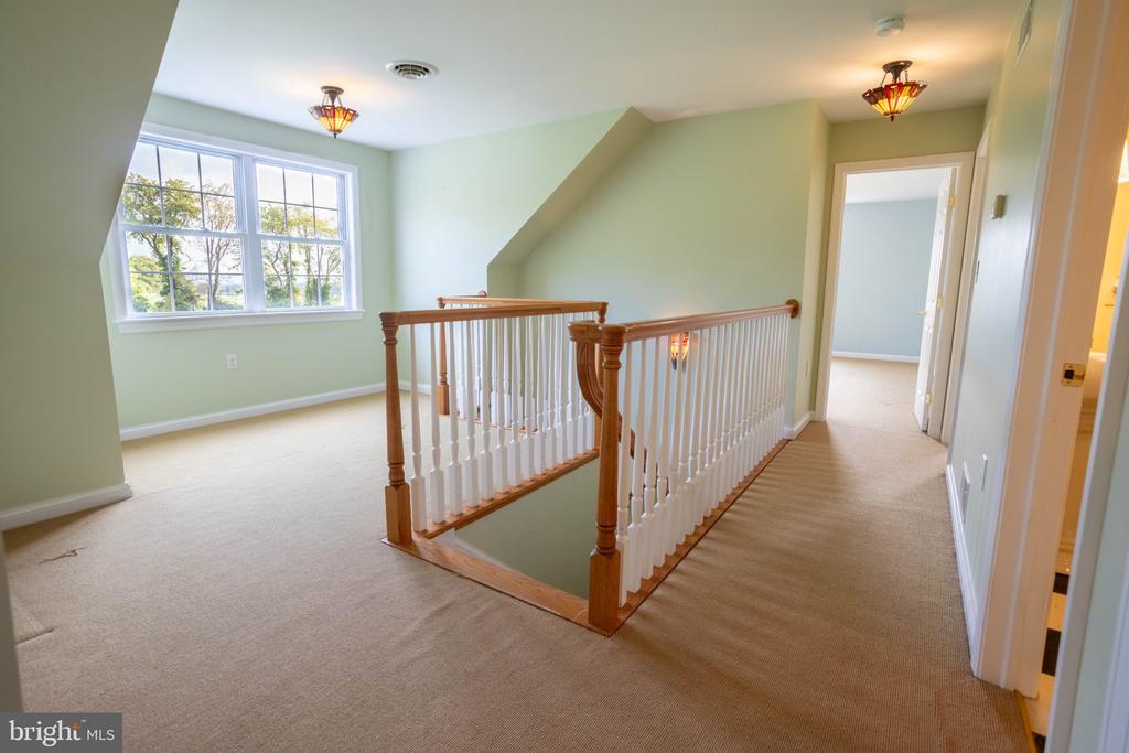 Upstairs landing with beige carpet, wood-and-white stair railing, and a large multi-pane window.