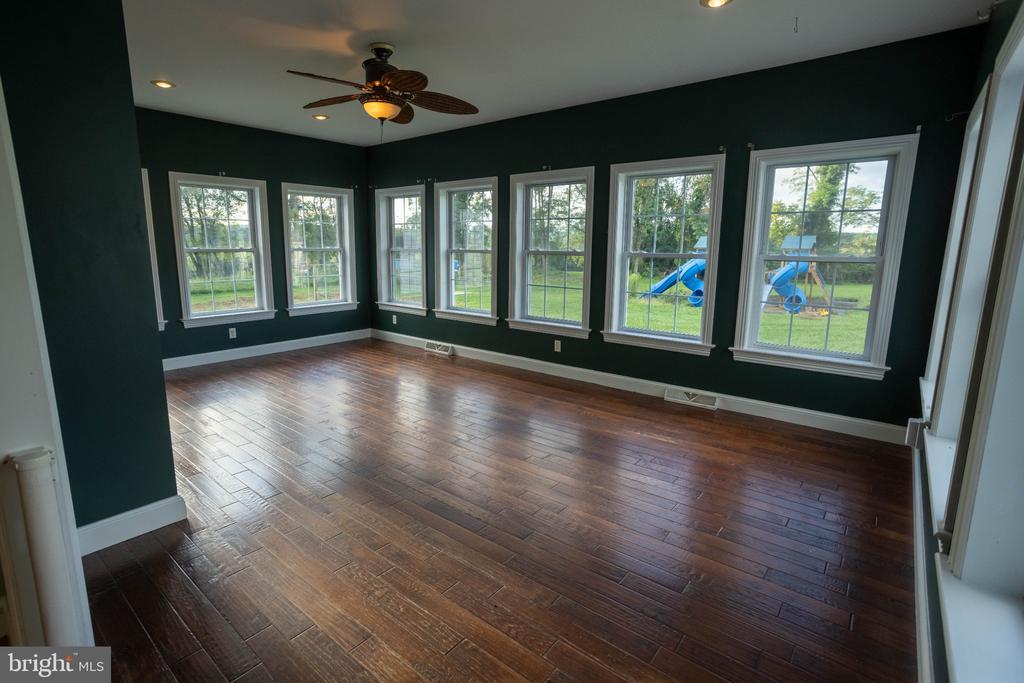 Empty room with dark green walls, polished wood flooring, and multiple windows overlooking a yard.
