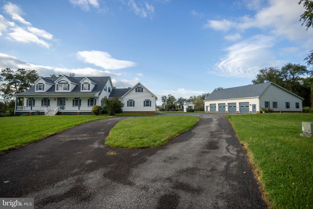 House with dormers and wraparound porch beside a detached multi-bay garage and curving driveway.