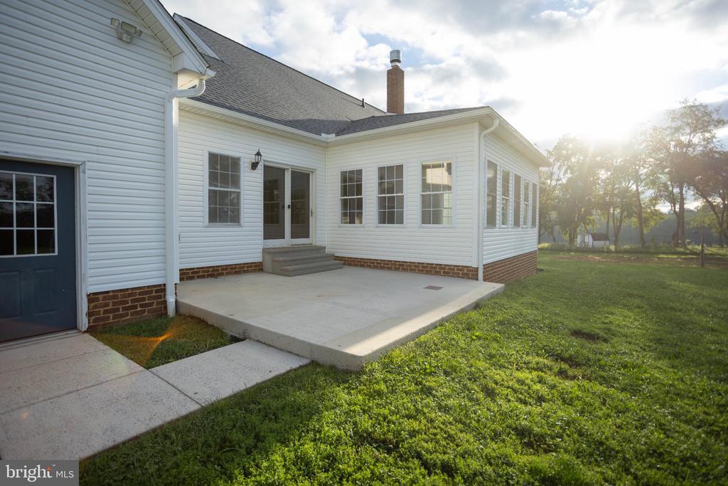 Rear exterior of a white-sided home with a concrete patio and enclosed sunroom.