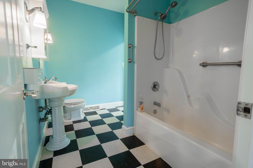 Bathroom with turquoise walls, checkerboard floor, pedestal sink, and white tub-shower.