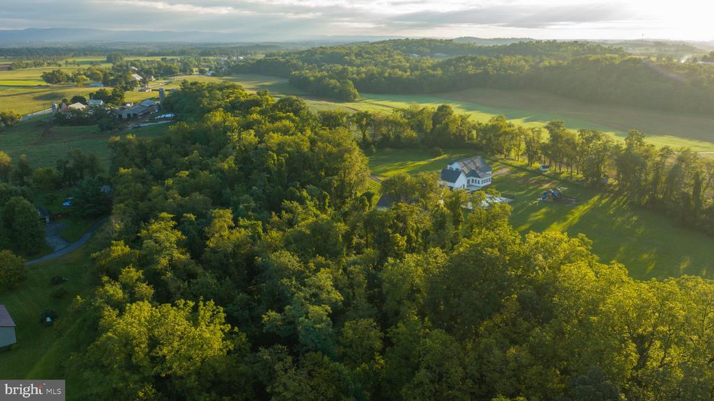 Aerial view of a home surrounded by wooded acreage, fields, and rolling countryside.