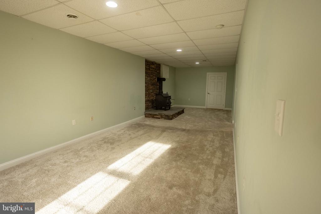 Vacant carpeted room with a wood stove on a raised stone hearth.