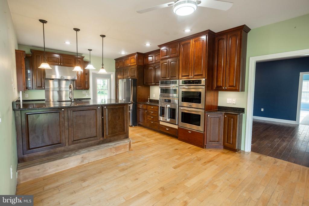Kitchen with dark cherry cabinets, stainless steel double ovens, a large island, and light hardwood floors.