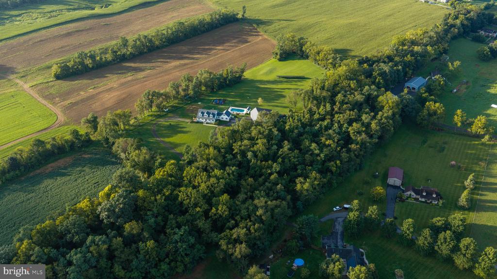 Aerial view of a white house and swimming pool amid wooded grounds and farmland.