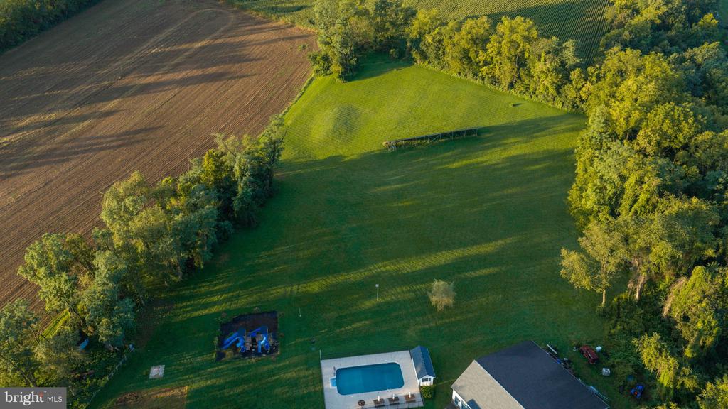 Aerial view of a large grassy yard with mature trees, farmland, and a swimming pool.