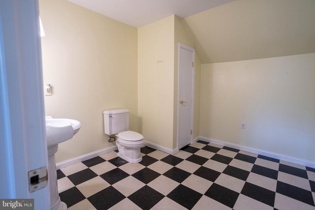 Empty bathroom with a checkerboard floor, white toilet, and partially visible pedestal sink.