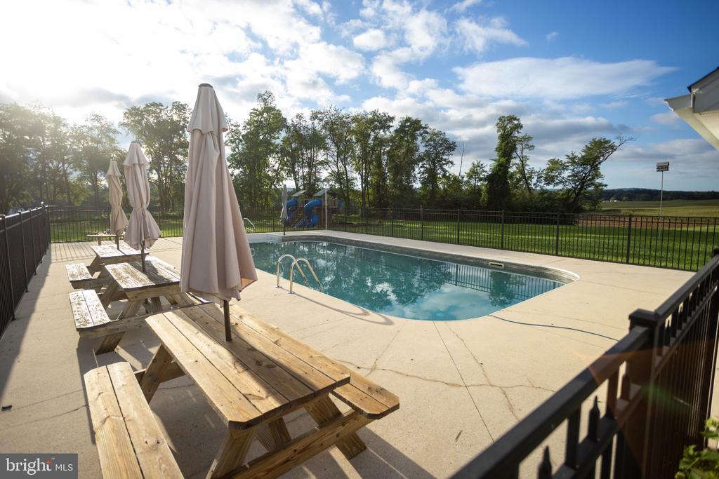 Outdoor pool with a concrete deck, picnic tables, and closed umbrellas.