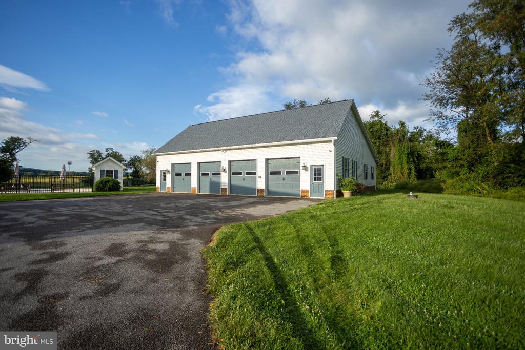 White detached garage with four blue-gray overhead doors beside a paved driveway and lawn.
