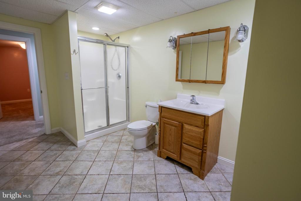 Bathroom with a glass shower, wooden vanity, framed mirror, and large square tile floor.