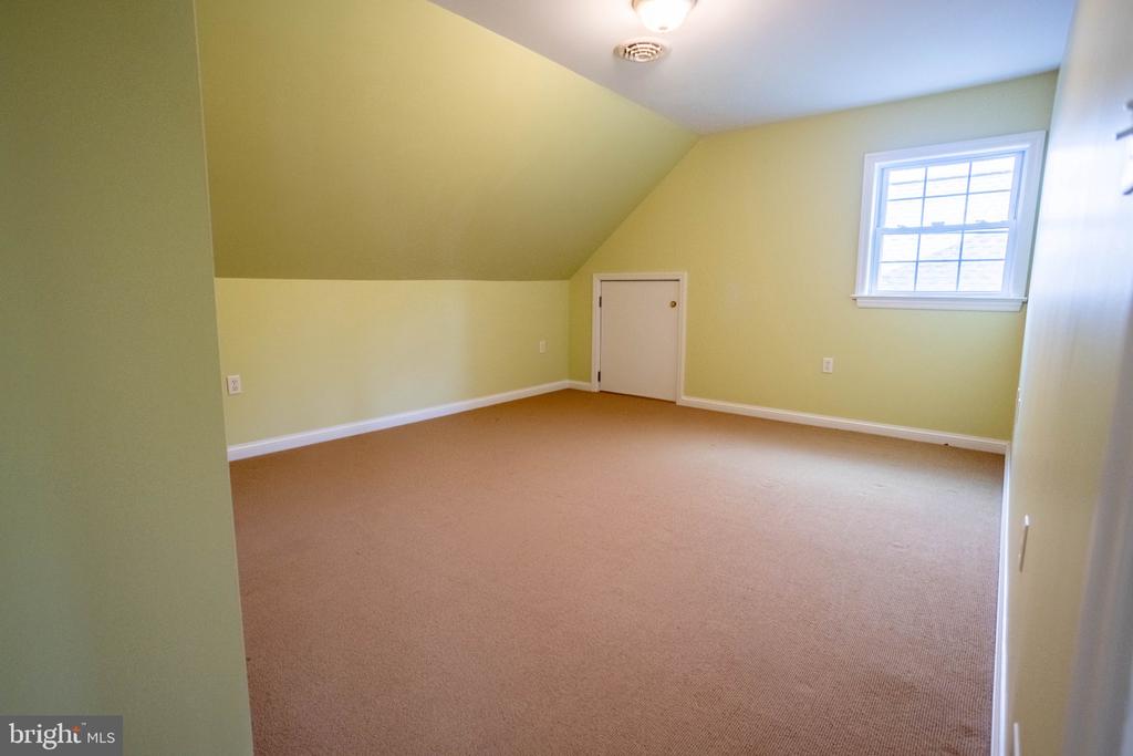 Empty upstairs room with a sloped ceiling, beige carpet, pale green walls, and a window.