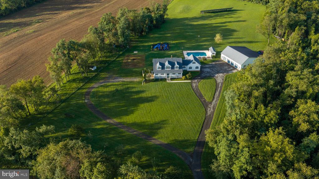 Aerial view of a home with a swimming pool, detached outbuilding, and expansive tree-lined lawn.