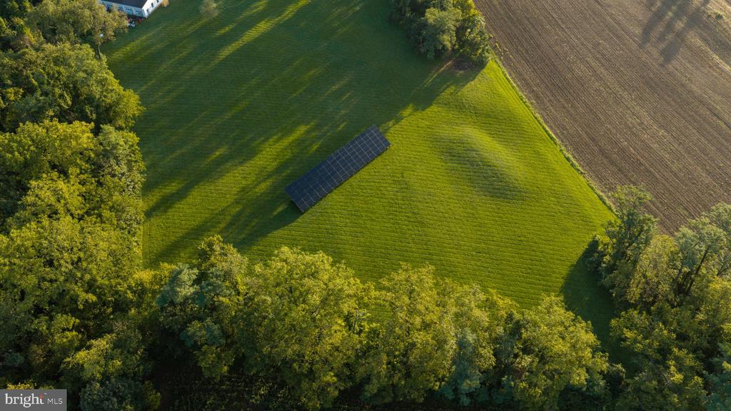 Aerial view of a tree-lined green property with a long solar panel array.