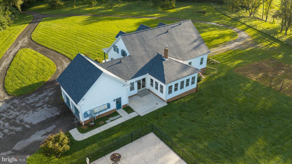 Aerial view of a white multi-wing house with a gray roof and curving driveway.