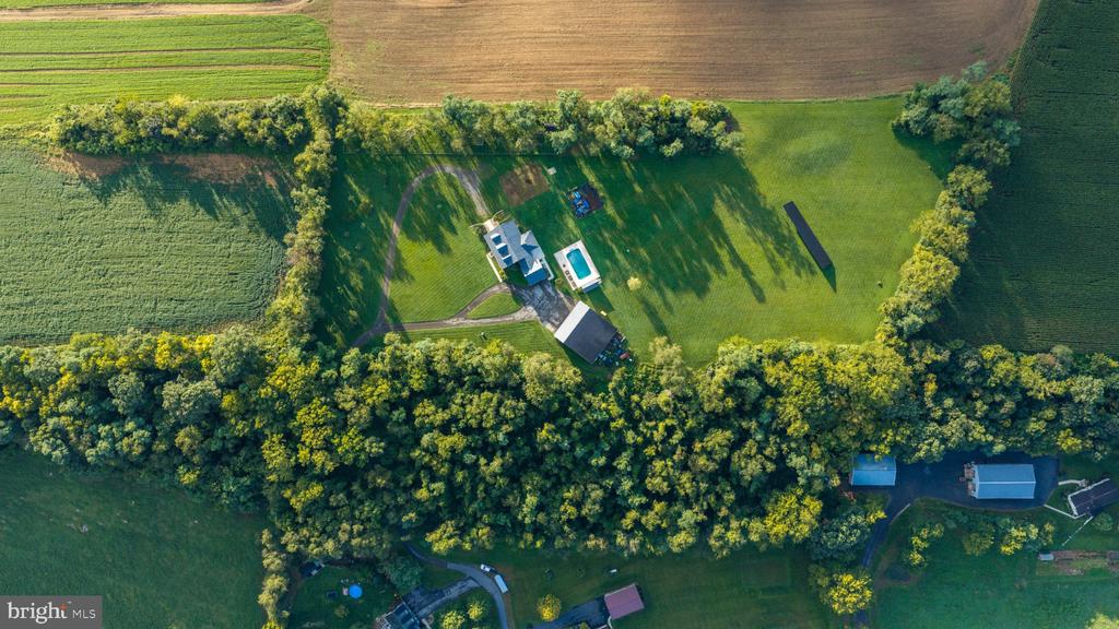 Aerial view of a home and swimming pool amid tree-lined acreage and surrounding farmland.
