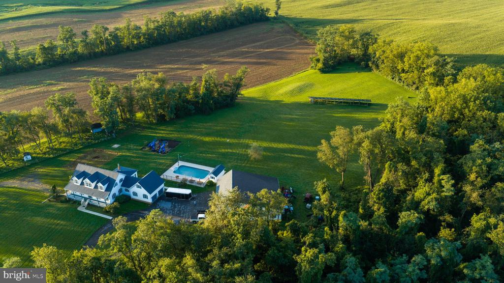 Aerial view of a white house with a swimming pool, expansive lawns, trees, and surrounding fields.