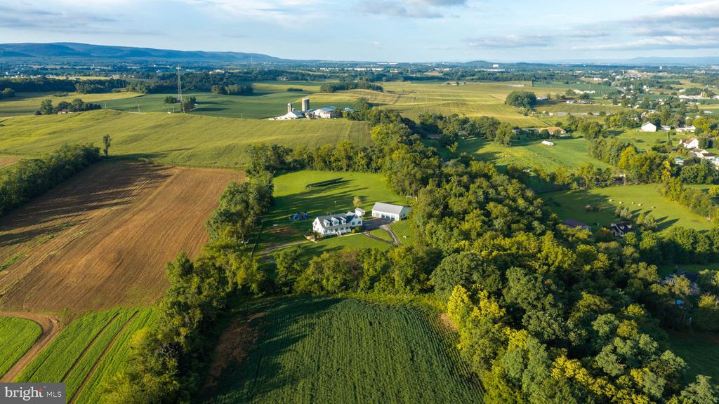 Aerial view of a rural home surrounded by farmland, trees, and outbuildings.