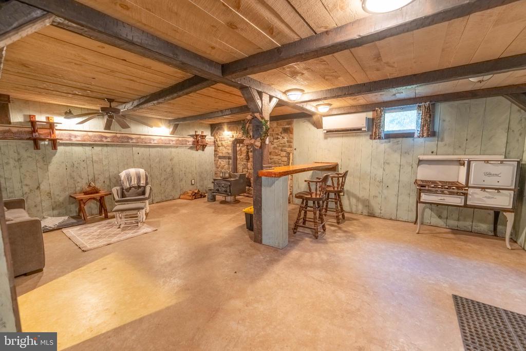 Basement recreation room with exposed beams, stone stove surround, and raised bar.