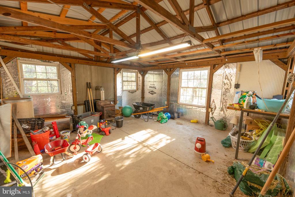 Cluttered workshop with exposed wood framing, concrete floor, three windows, tools, and toys.