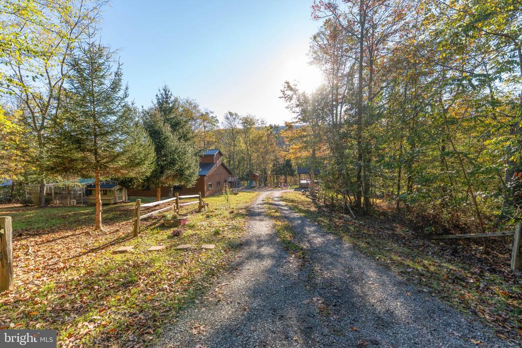 Gravel driveway leads to a brown house and outbuildings among autumn trees.